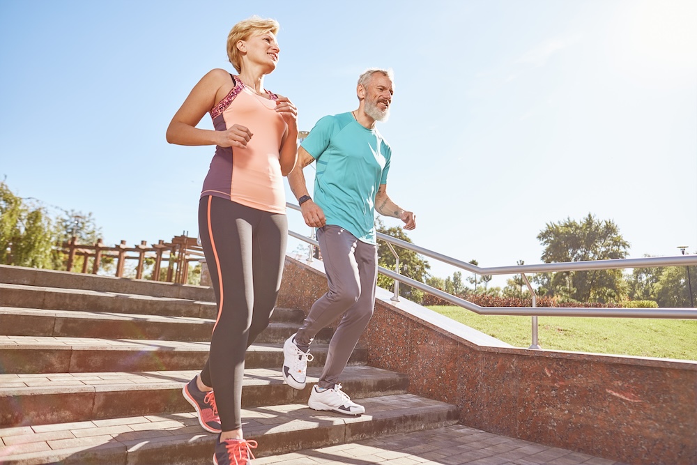 A senior couple jogs happily together down outdoor steps in a sunny park, staying active and healthy - Alan Dayan, MD, PC, FAAOS A senior couple jogs happily together down outdoor steps in a sunny park, staying active and healthy - Alan Dayan, MD, PC, FAAOS